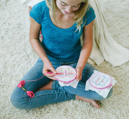 Child using embroidery kit fabric and hoop, stitching a butterfly pattern
