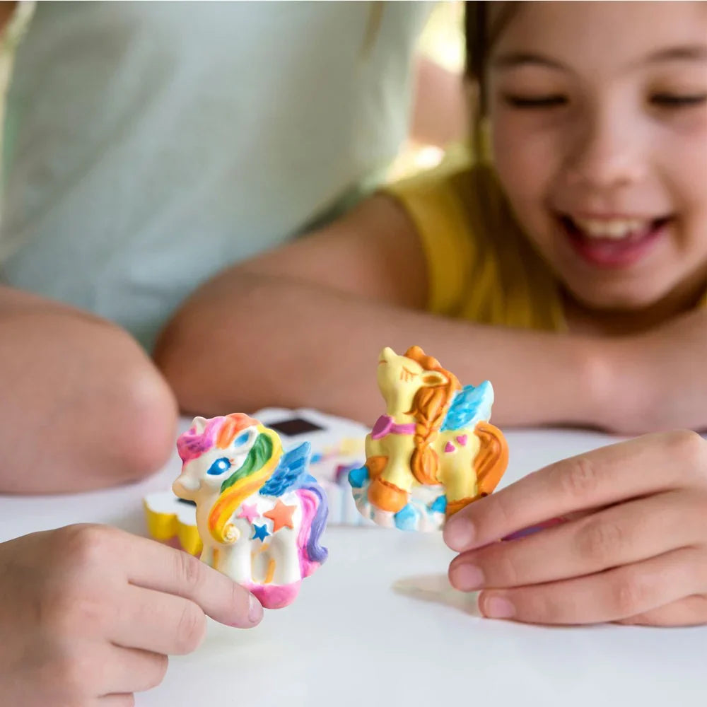 Child hands assembling small rainbow unicorn figurines on white surface