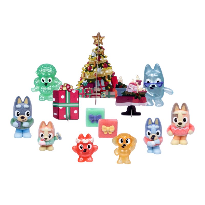 A collection of colorful, glossy dog-shaped holiday figurines and matching gift boxes arranged around a decorated Christmas tree on a plain white background.